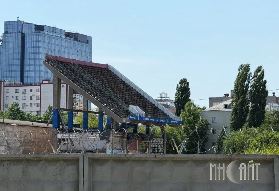 Демонтаж Восточной трибуны приостановлен: подрядчик выполнил почти все работы, но два кирпичных гаража связаны с конструкцией трибуны, из‑за чего нельзя применять тяжёлую технику. Выкуп участков затянулся — единственный законный путь теперь через суд.