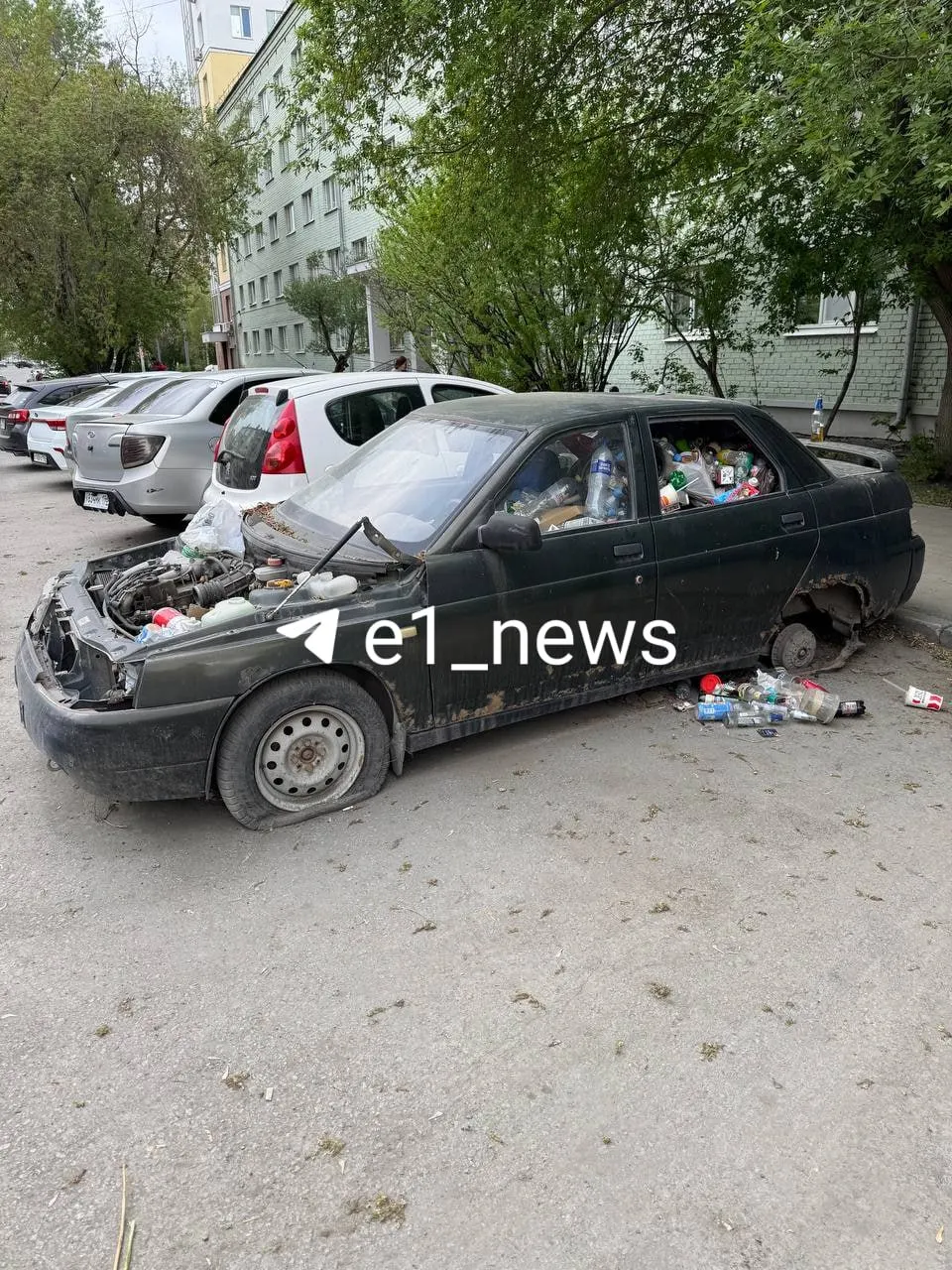Автомобиль у общежития на улице Большакова, 79 заполнен пакетами с бытовым мусором и упаковками; прохожие опасаются за безопасность, а сами действия могут расцениваться как порча имущества или несанкционированная свалка.