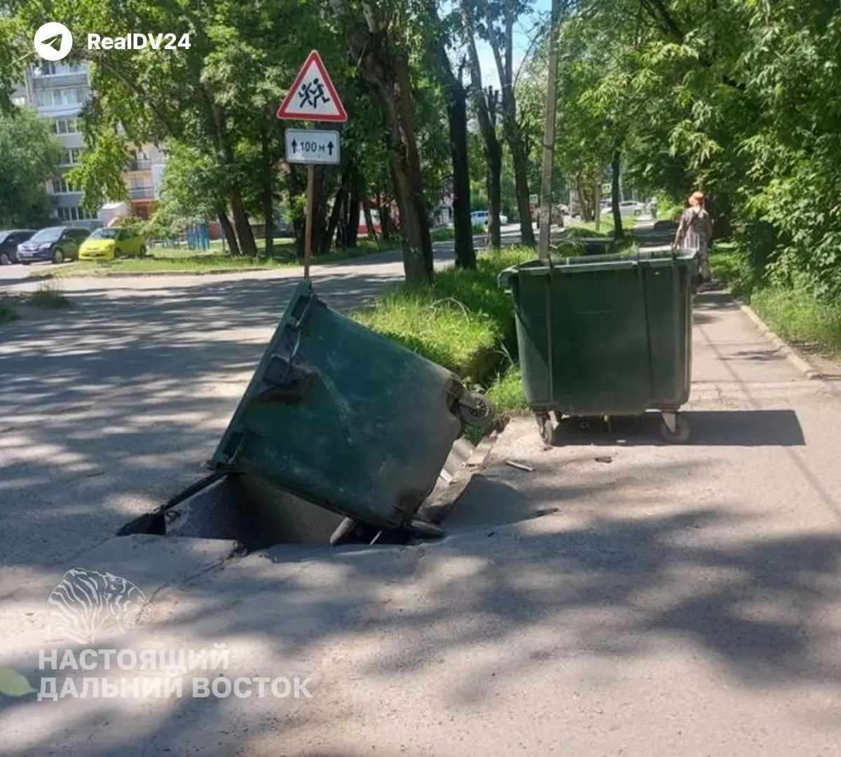В районе ДОСов в Хабаровске провалившийся асфальт закрыли мусорным баком и ещё несколькими контейнерами, размещёнными посреди проезжей части. Из‑за этого мусоровоз не может подъехать, отходы гниют на жаре, а жители жалуются, что обращения остаются без реакции.