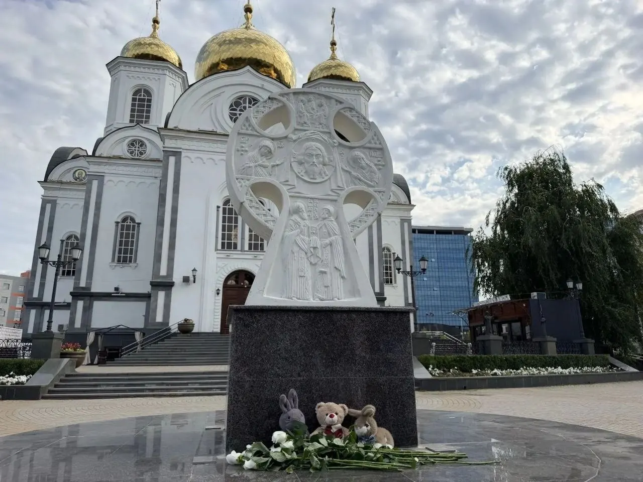 Люди возлагают цветы, свечи и игрушки к поклонному кресту возле собора Александра Невского на улице Постовой.